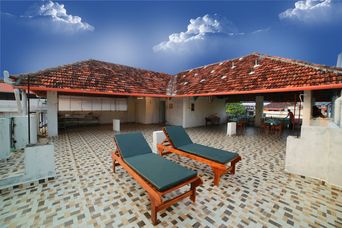 Open rooftop terrace with a patterned grey-and-cream tiled floor, two wooden sun loungers with dark green cushions and a covered area under red-tiled roofs.