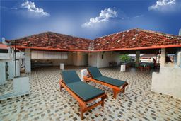 Open rooftop terrace with a patterned grey-and-cream tiled floor, two wooden sun loungers with dark green cushions and a covered area under red-tiled roofs.