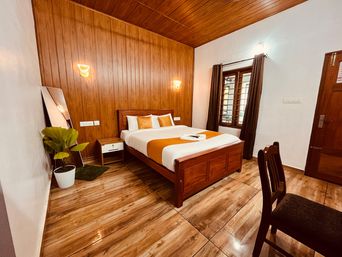 Bedroom with wood-panelled walls and ceiling, a double bed with an orange runner and white bedding, wall lights, a small wooden bedside table and a potted plant.