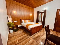 Bedroom with wood-panelled walls and ceiling, a double bed with an orange runner and white bedding, wall lights, a small wooden bedside table and a potted plant.