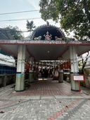 A covered entrance to a building with a tiled floor and pillars, featuring a decorative archway with a central figure flanked by two animal statues, and a sign with text above the entrance.
