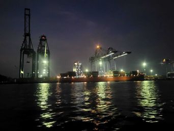 Container ship being loaded at night under illuminated gantry cranes.