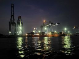 Container ship being loaded at night under illuminated gantry cranes.