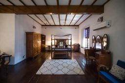 Large room with dark timber floors and exposed beams, a four-poster bed at the back, a carved wooden wardrobe, and a three-mirror dressing table.