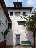 The synagogue’s white clock tower with a round clock face and weathervane, a bougainvillea and green bench below it.