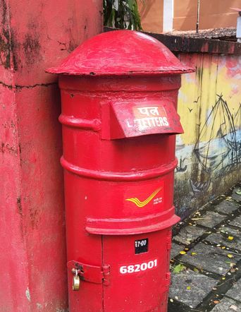 Red India Post pillar letterbox marked ‘682001’ with a boat mural on the wall behind