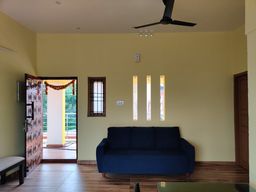 Living room with pale yellow walls, a navy three-seater sofa on a wood floor, a ceiling fan, and a carved wooden door open to a balcony.