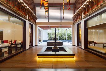 Central courtyard with a tall brass lamp stand over a sunken pool on a timber deck, glass-walled rooms with sofas on each side, and a garden beyond.