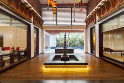 Central courtyard with a tall brass lamp stand over a sunken pool on a timber deck, glass-walled rooms with sofas on each side, and a garden beyond.