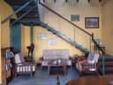 A cafe seating area with floral-upholstered sofa and armchairs below a blue open staircase, framed pictures on a yellow wall.