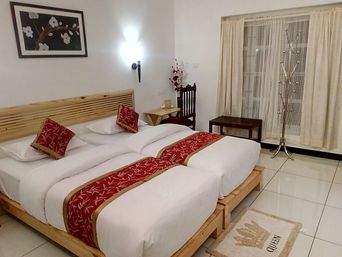 Room with two wooden beds with white bedding and red-patterned runners, a slatted wooden headboard, cream curtains, and a chrome coat stand.