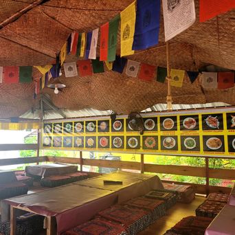 Restaurant seating under a bamboo ceiling hung with Tibetan prayer flags, photo-menu banner on the wall.