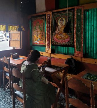 Restaurant interior with a diner seated below Buddha and deity tapestries on a green wall