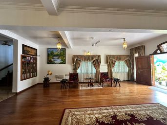 Large living room with a polished wood floor, two red upholstered armchairs by a small round table, patterned curtains, and a wall display cabinet.